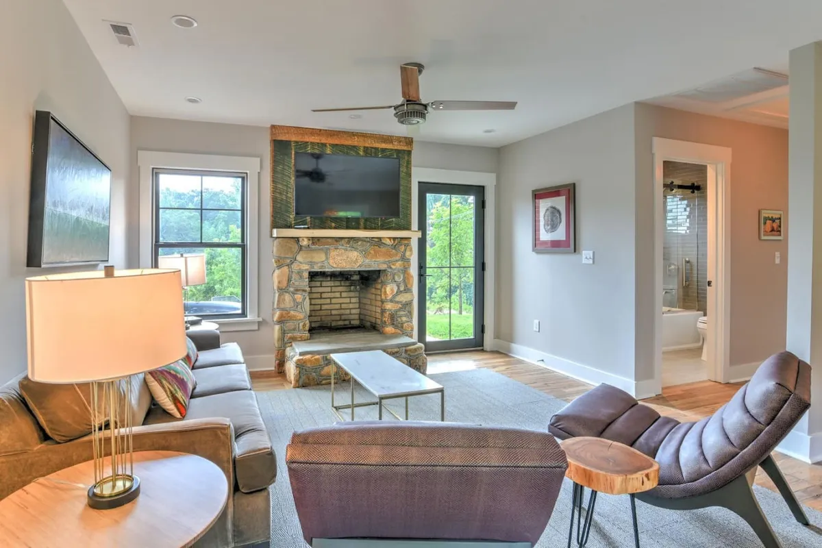 A comfortable seating area arranged around a stone fireplace, with large windows offering scenic views, modern light fixtures, and a relaxed atmosphere—perfect for unwinding, reading, or intimate conversation.