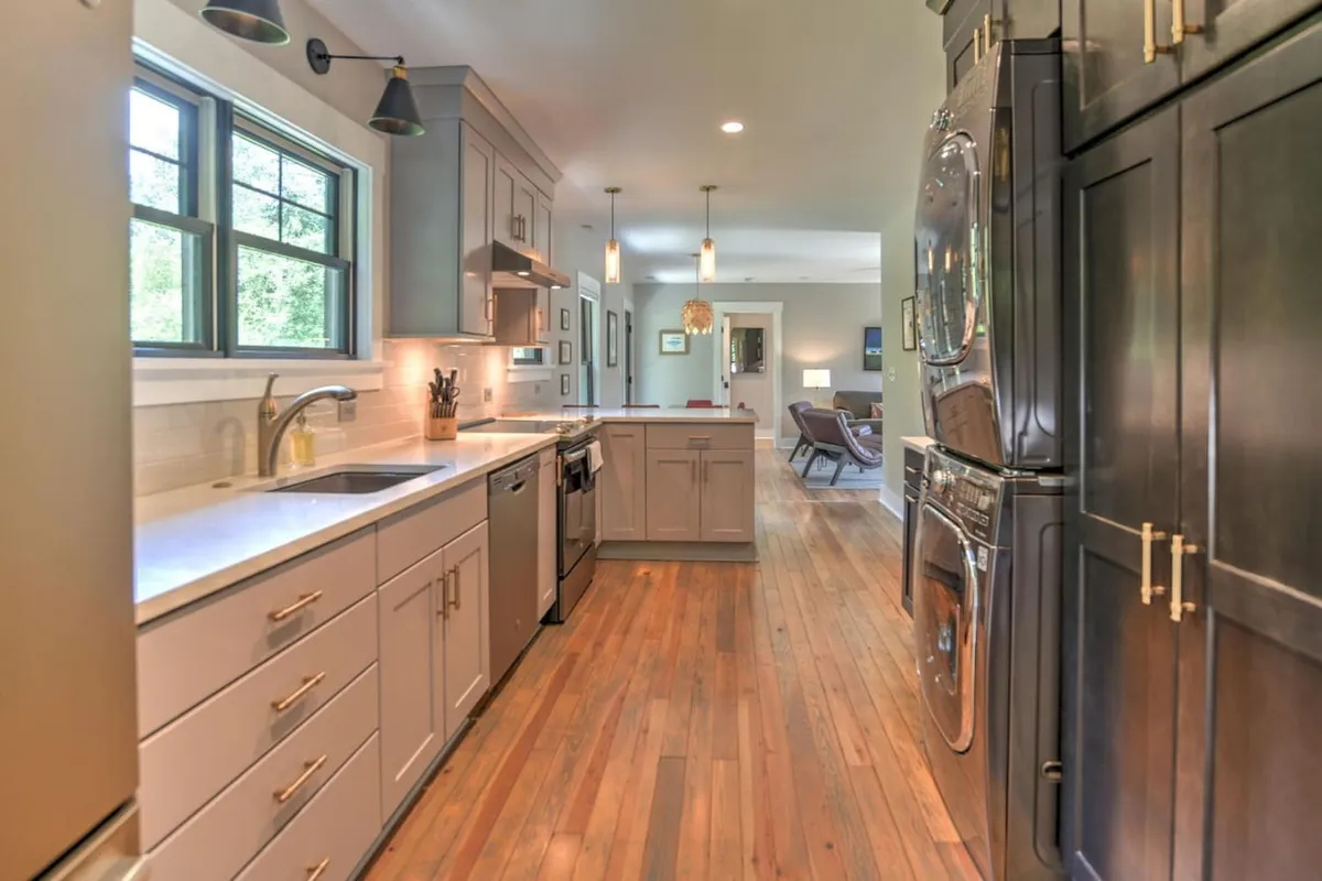 A spacious, inviting kitchen with a large island, gleaming stainless steel appliances, and rich wood flooring. The layout suggests ample space for groups to gather, cook, and connect, with warm lighting contributing to a welcoming ambiance.