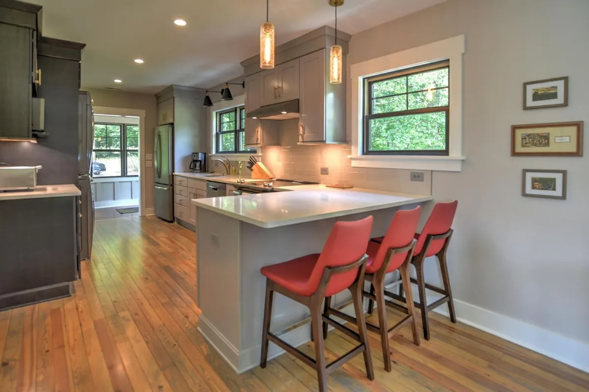 An inviting kitchen area with an island countertop, vibrant red bar stools, and stylish modern fixtures. Windows usher in natural light, creating a warm atmosphere ideal for cooking, entertaining, and casual family gatherings.