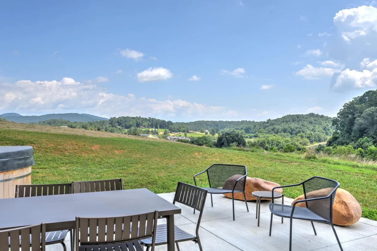 An elegant exterior dining area with a modern dining table and chairs, unique rock seating, and an expansive view of the surrounding hills. The peaceful mood is enhanced by the golden hour light, ideal for morning coffee or evening gatherings.