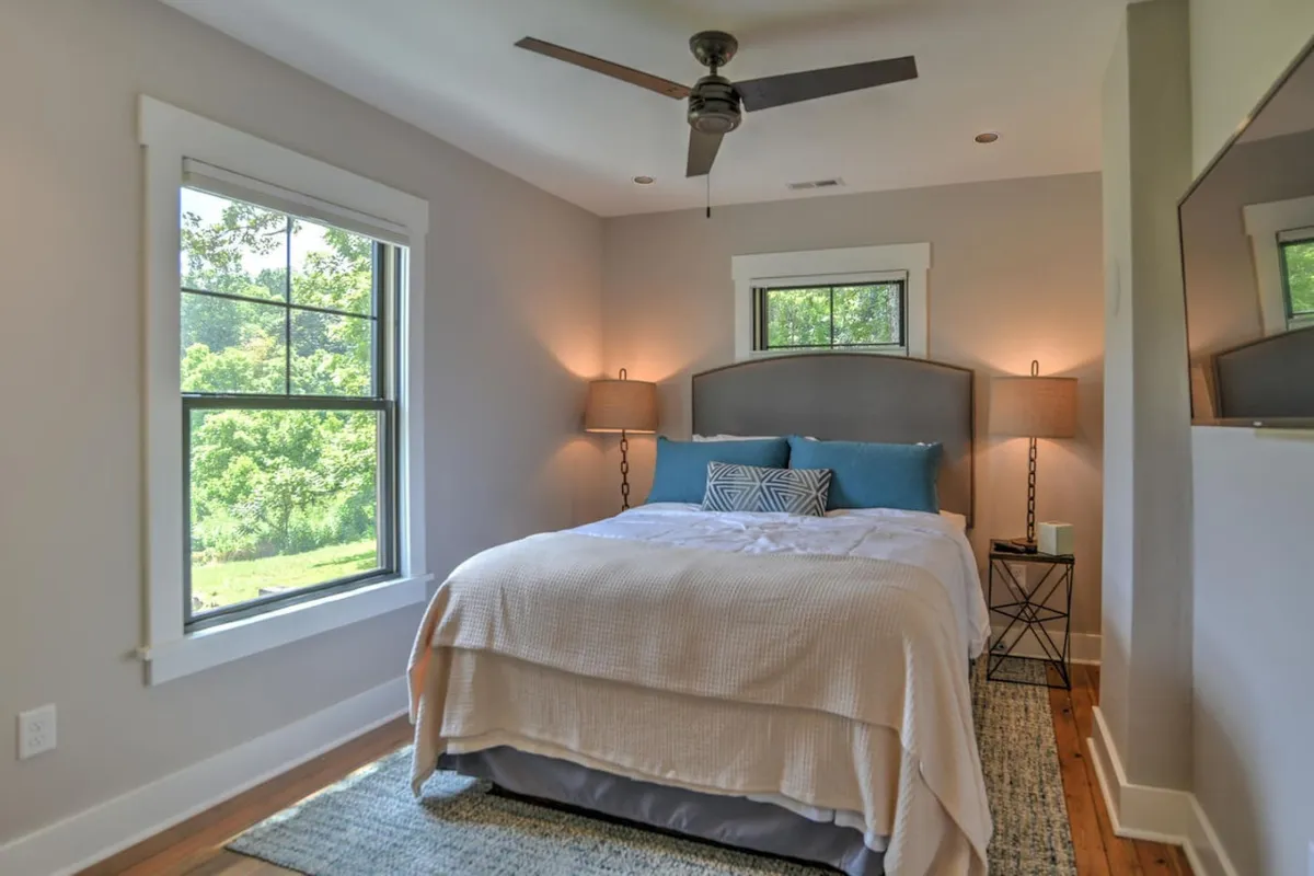A tranquil bedroom with a comfortable bed, windows letting in natural light, elegant nightstands, and decorative pillows. The space is bathed in soft daylight, creating an inviting environment for relaxation and rejuvenation.