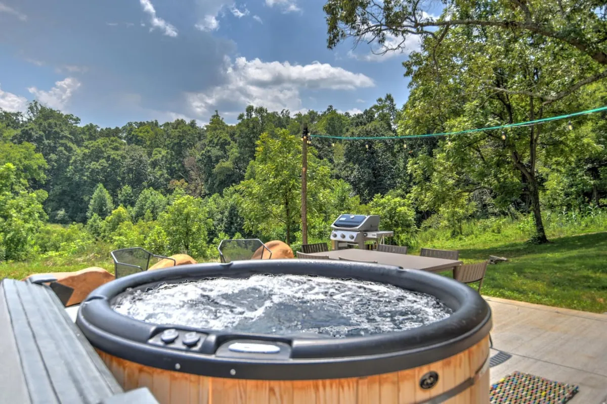 A tranquil outdoor scene featuring a hot tub nestled among lush greenery, with a grill nearby. The setup offers a private, peaceful retreat surrounded by nature—perfect for unwinding after a day of exploration.